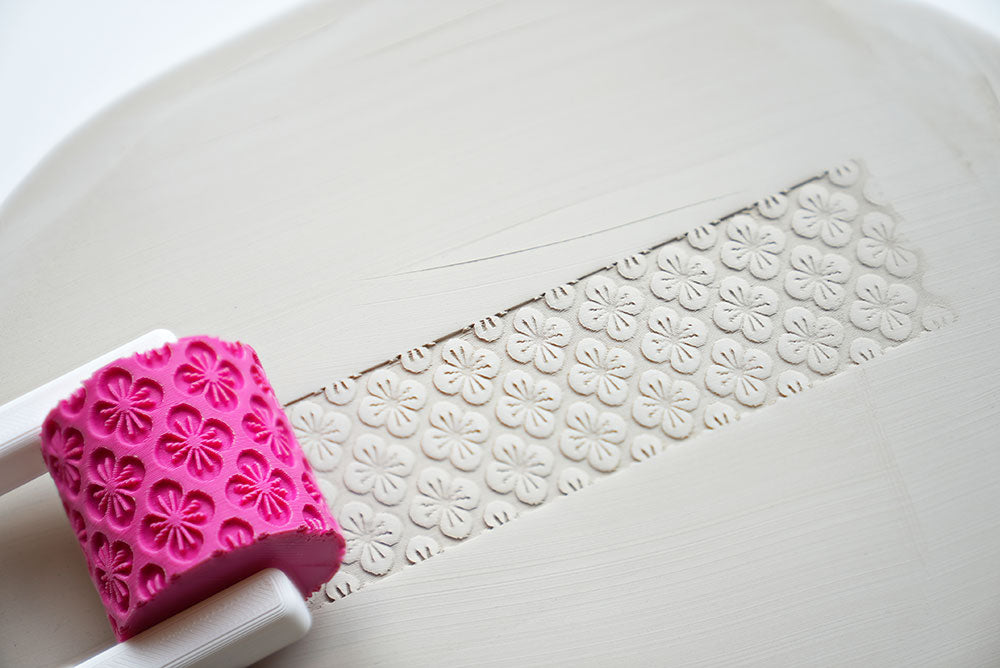 Texture roller for pottery with handle on a white surface, showing pattern detail