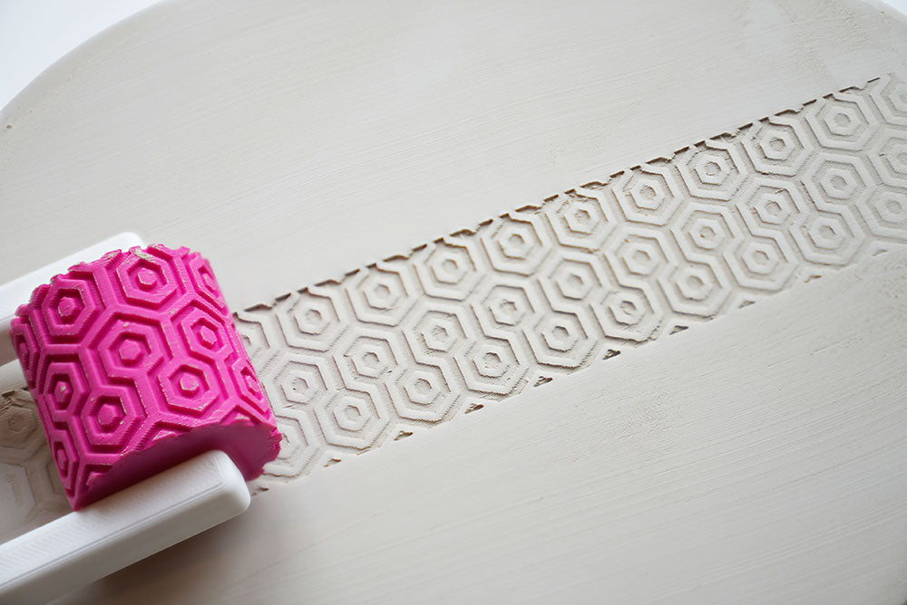 Texture roller for pottery with handle on a white surface, showing pattern detail