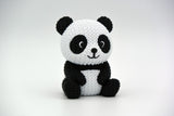 Knitted panda figure styled on a wooden shelf next to plants and neutral home decor